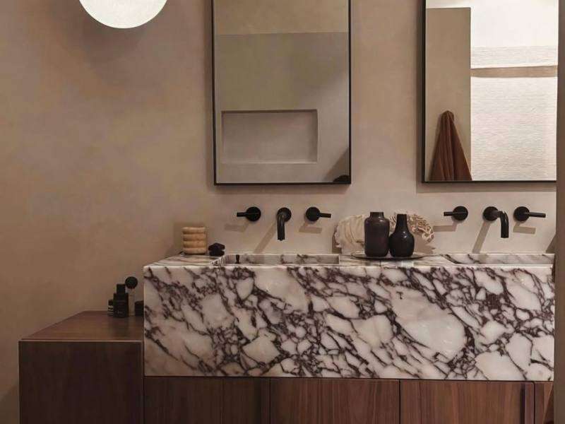 legant bathroom finished in Meoded Concretta plaster in a soft, sandy beige custom color, creating a warm, neutral backdrop that highlights the striking marble sink and custom-designer mirrors.